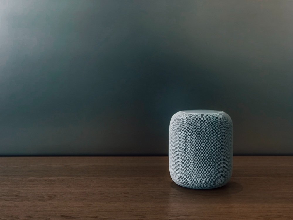 Smart speaker on wooden table against a dark background, representing modern technology in photography and video contexts.
